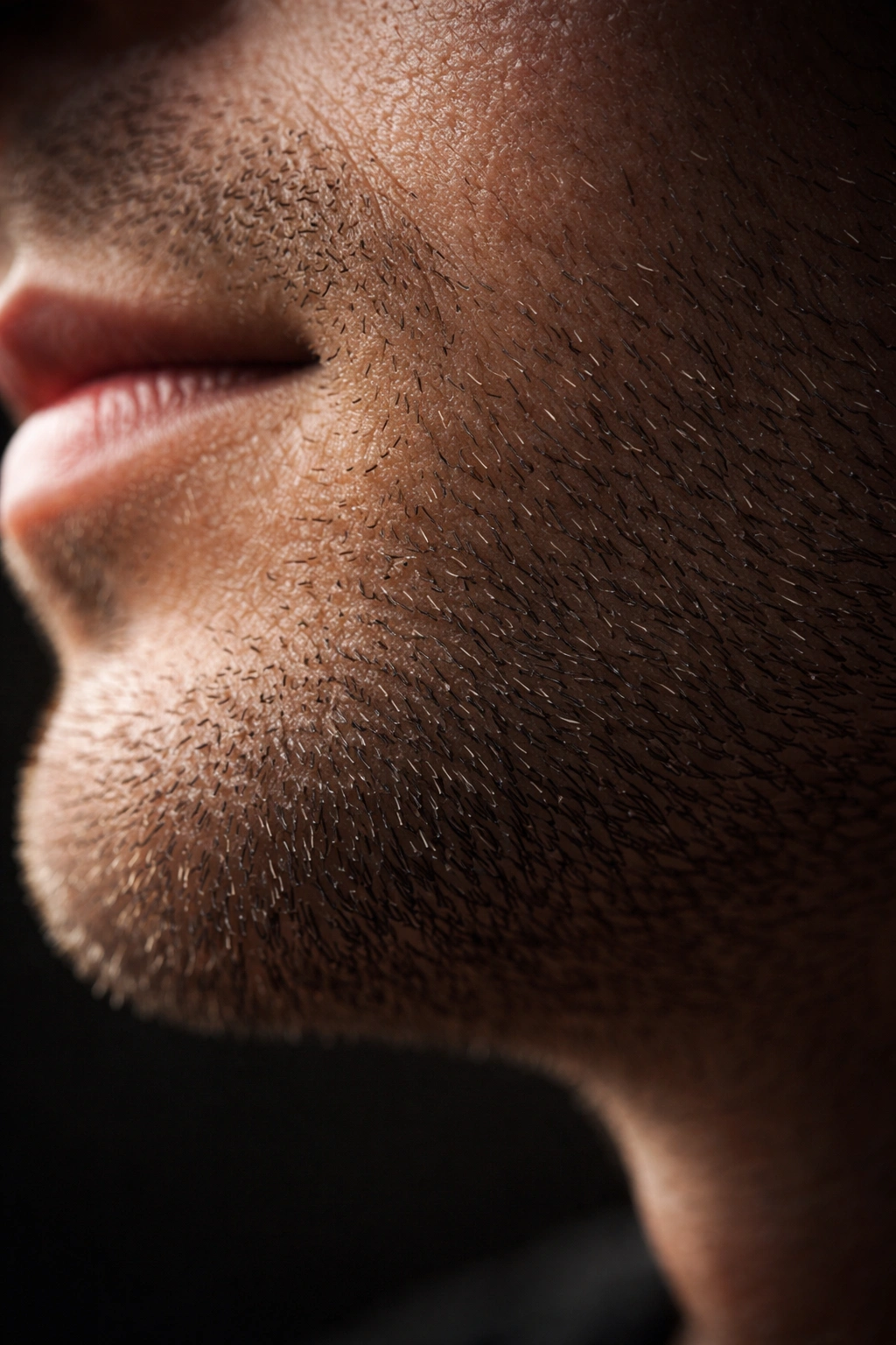 Jawline with stubble of varying lengths under dramatic lighting