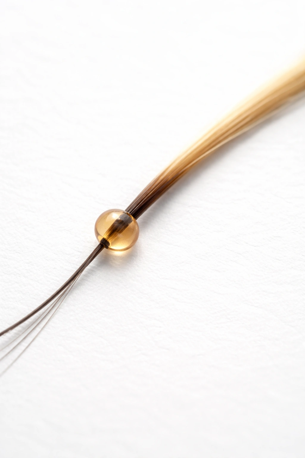 Hair strand with bead used to mark growth on white surface