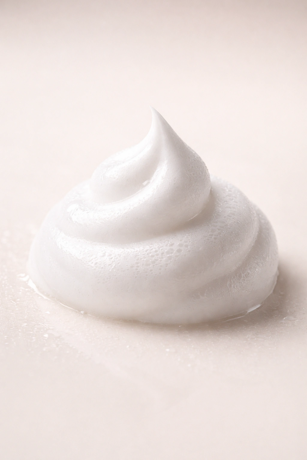 Foamy dollop of hair mousse with glossy sheen on neutral background