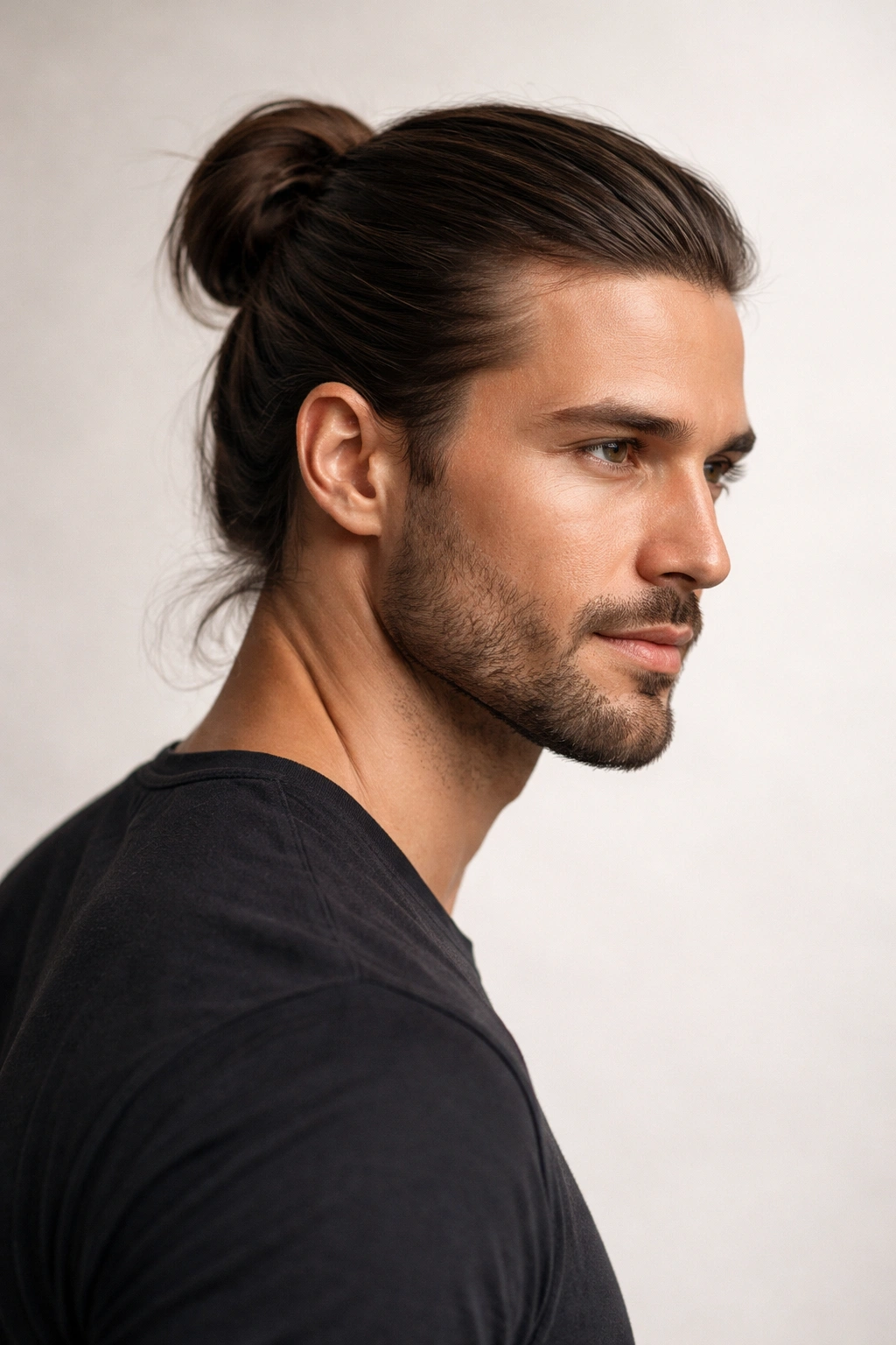 Close-up of a man with a classic bun on shoulder-length hair against a neutral backdrop
