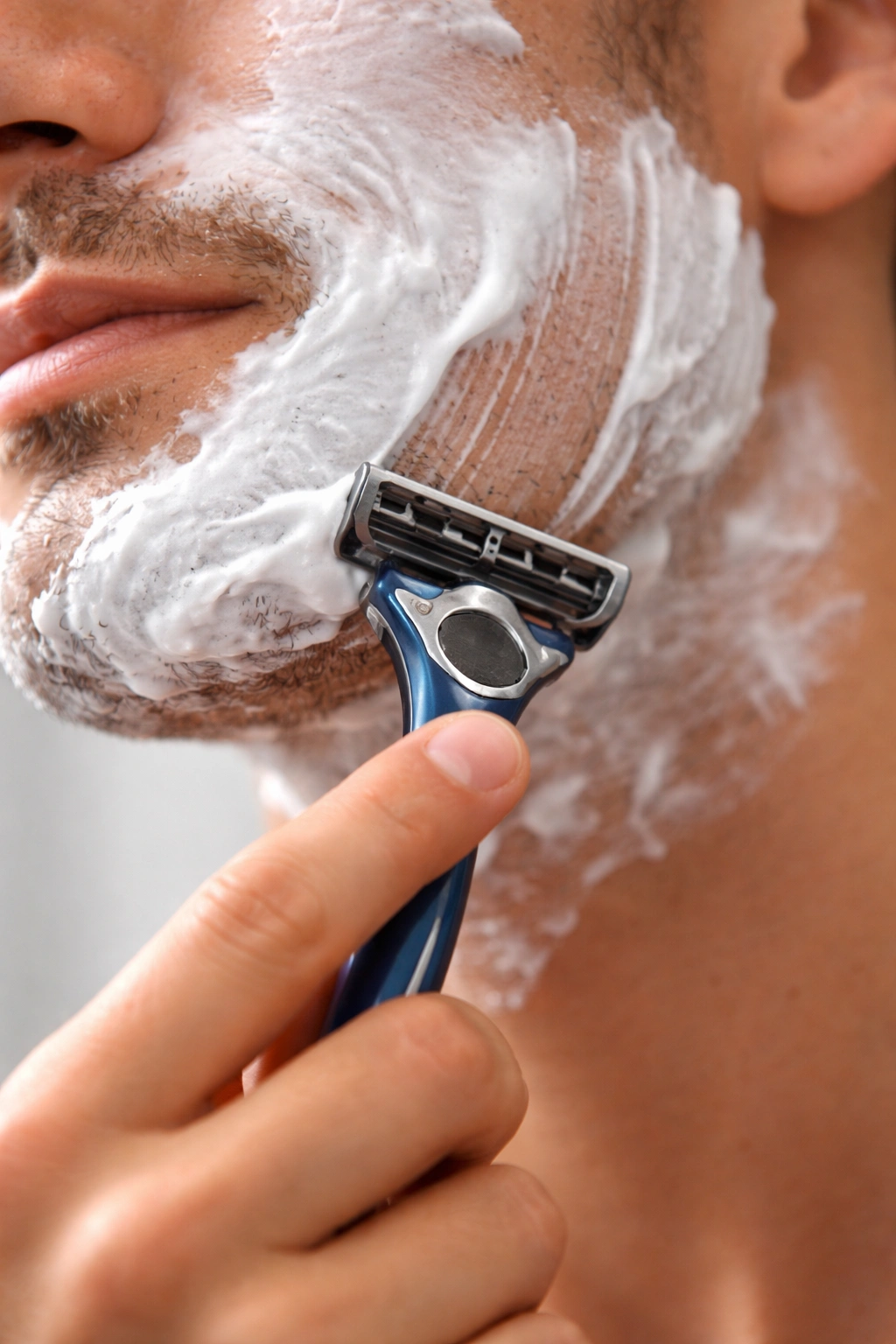 Close-up of hand and razor on damp skin during shaving